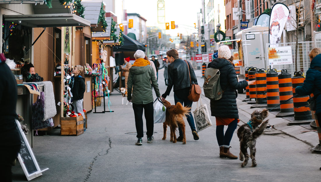 People with pets on leashes walk through a holiday fair.