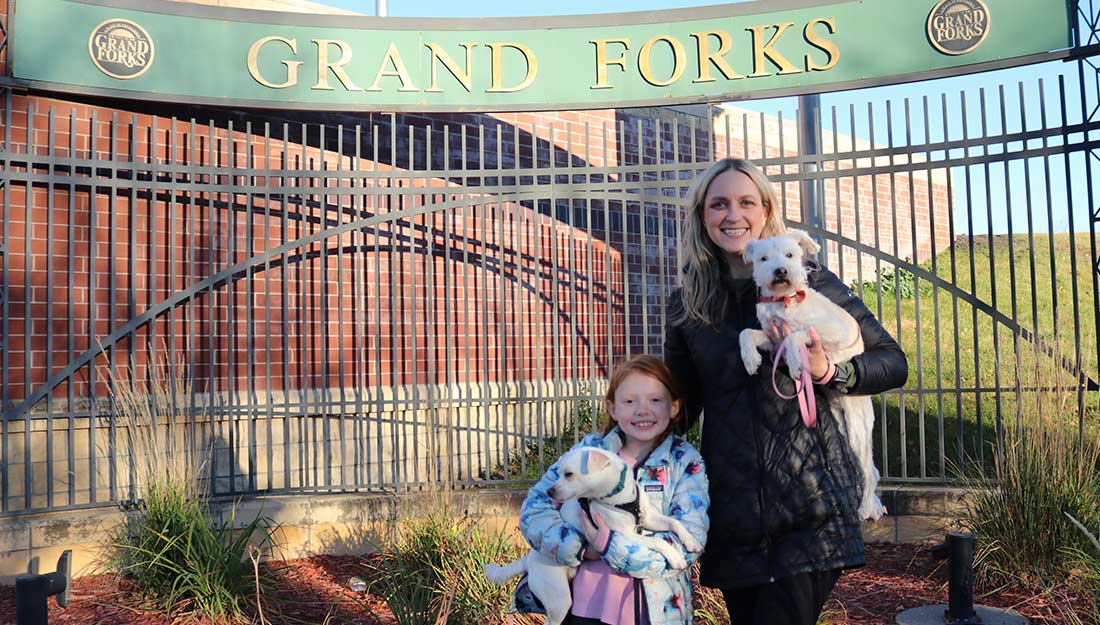 People stand with pets below the Grand Forks sign